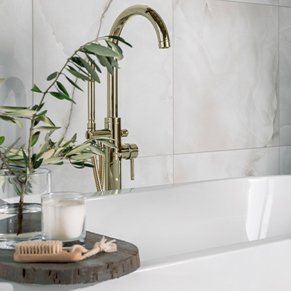 White sink with gold tap with marble style tiles on the wall